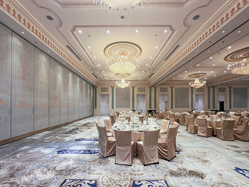 A spacious hotel ballroom with patterned carpet flooring, arranged banquet seating and elegant lighting.